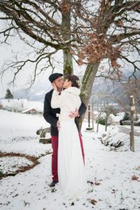 Les mariés s'embrassent emmitouflés dans leurs vêtements d'hiver pour ce mariage photographié en décembre près d'Annecy