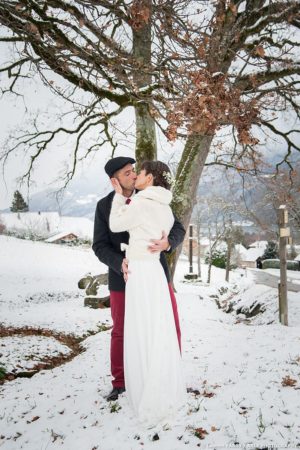 Le baiser des mariés près d un banc enneigé sous les arbres en hiver : photographe mariage Savoie