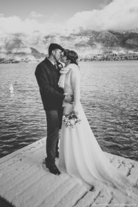Les mariés s'embrassent sur le ponton enneigé du lac d'Annecy (mariage en hiver, photo en sépia)