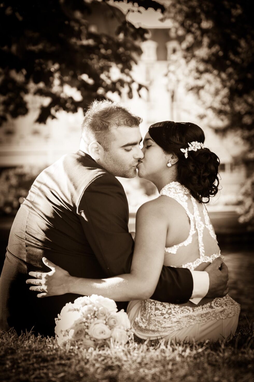 Photographe de mariage à Annecy : pose assise romantique des mariés devant l'Imperial Palace, en sépia