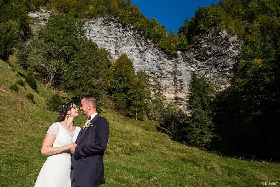 Reportage de mariage en automne à la montagne : photo des mariés sous la falaise et sa cascade