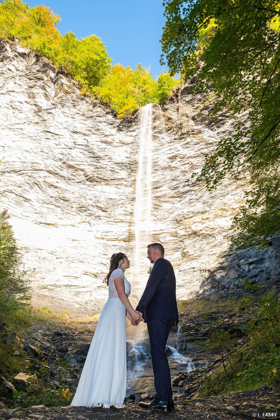 Reportage de mariage en automne à la montagne : photo couleurs des mariés en devant une cascade
