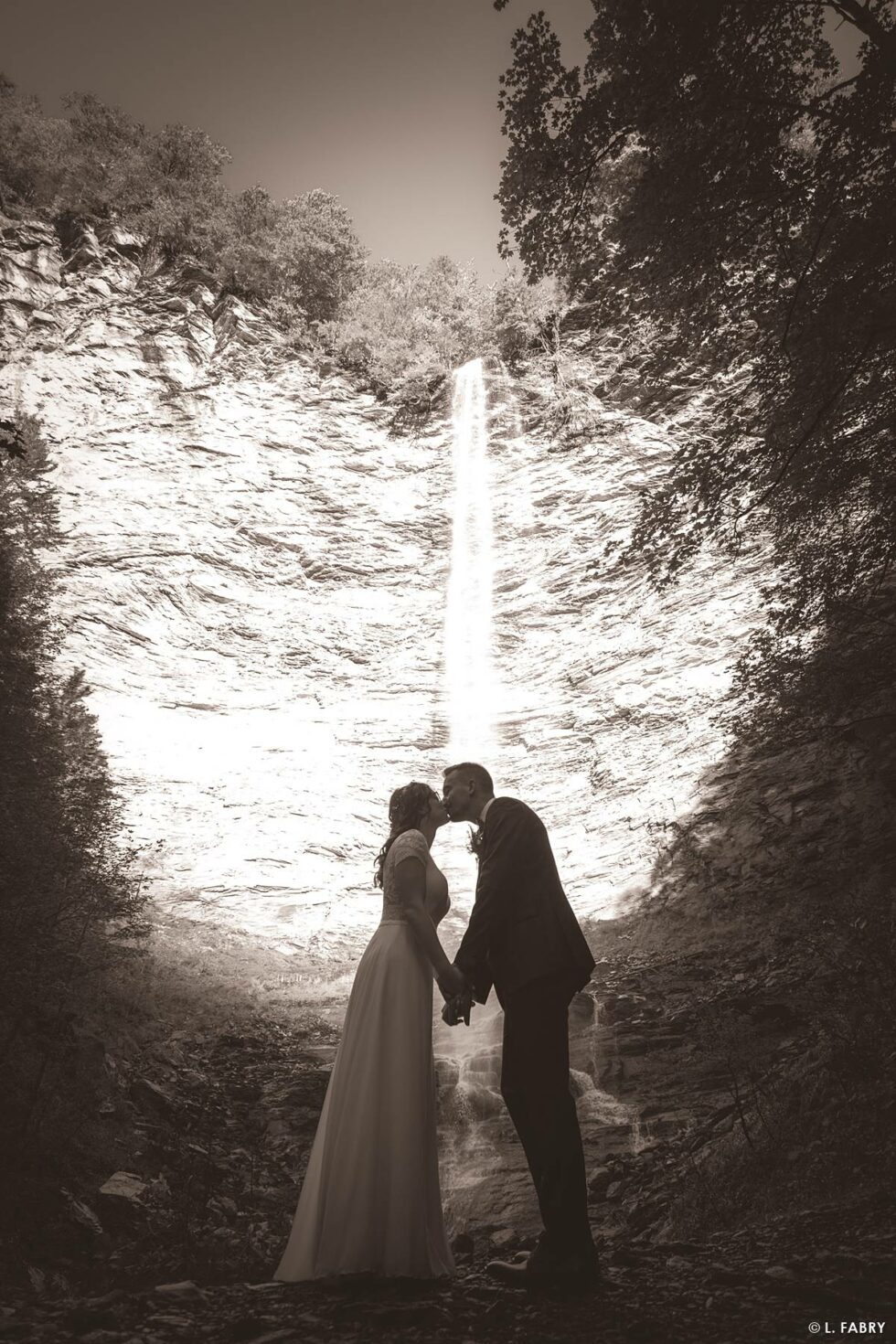 Reportage de mariage en automne à la montagne : photo sépia des mariés en devant une cascade