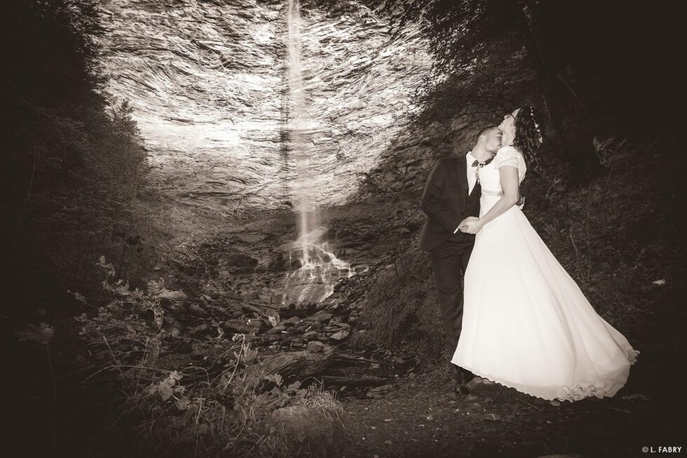 Reportage de mariage en automne à la montagne : photo des mariés en sépia devant la cascade