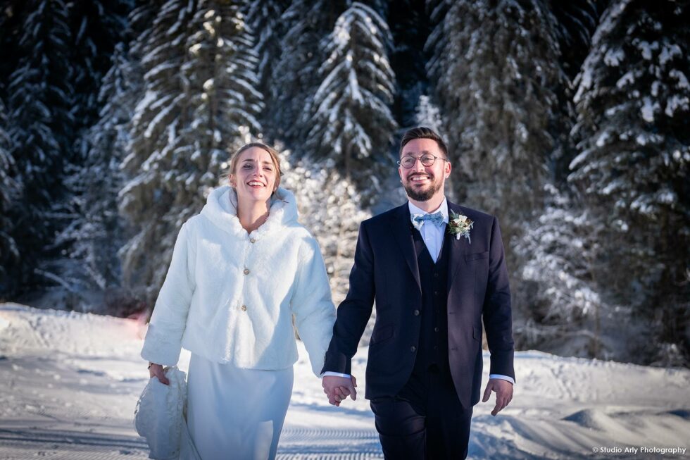 Mariage en hiver à la Giettaz : portrait des mariés se tenant la main devant des sapins enneigés