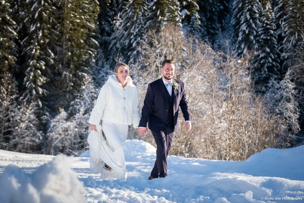 Mariage dans la neige en hiver : les mariés devant un décor de sapins enneigés